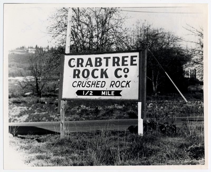 A sign that reads "Crabtree Rock Co. Crushed Rock in 1/2 mile". The back of the photo labels the sign as a monument to Donald "Don" E. Crabtree.