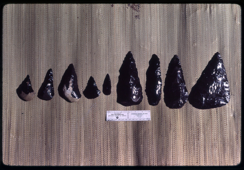 A photographic slide of a series of obsidian points accompanied by a measuring scale.