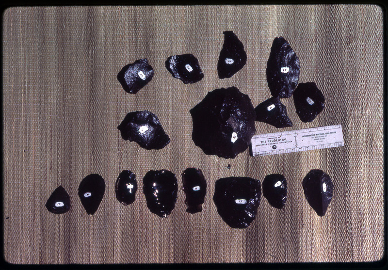 A photographic slide of a series of obsidian cores accompanied by a measuring scale.