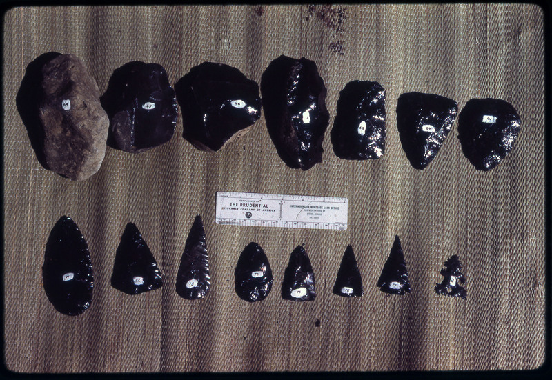 A photographic slide of a series of obsidian points and bifaces accompanied by a measuring scale.