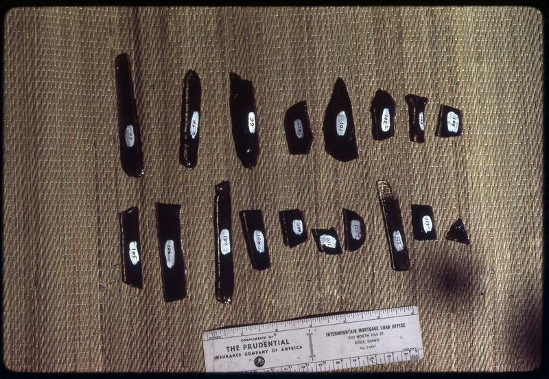 A photographic slide of a series of obsidian blades, points, and debitage accompanied by a measuring scale.