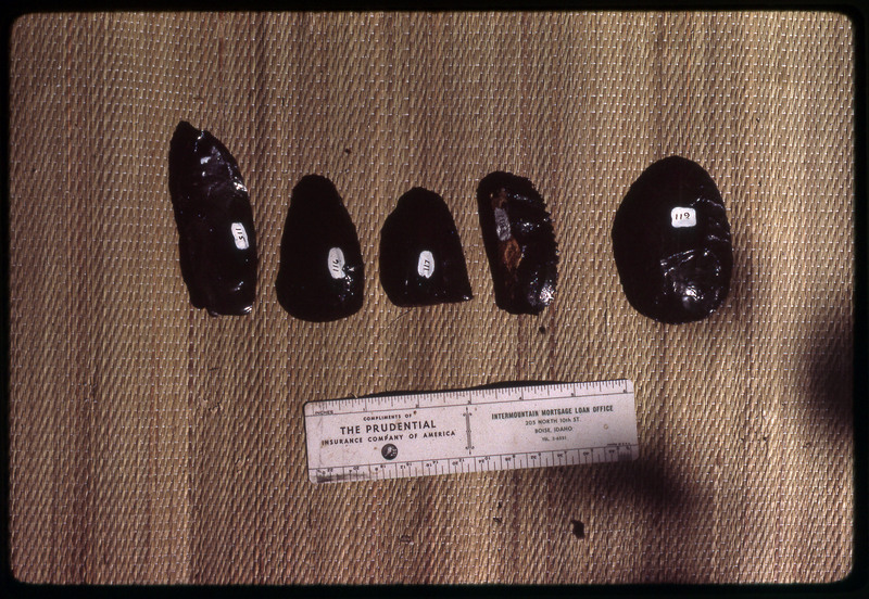 A photographic slide of a series of obsidian bifaces accompanied by a measuring scale.