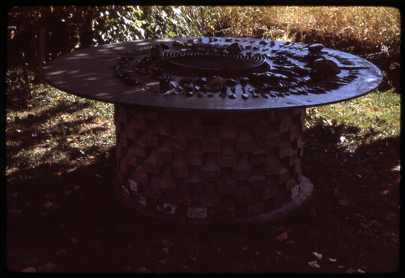 A photographic slide of a series of obsidian implements and flintknapping tools organized in concentric circles on a table.