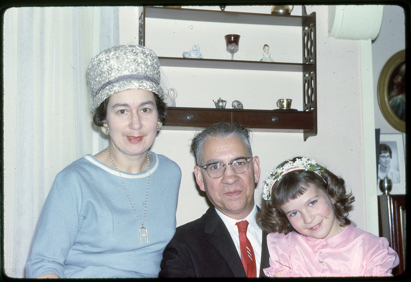 A photographic slide of a man, woman, and a young girl smile whilst dressed up for a party.