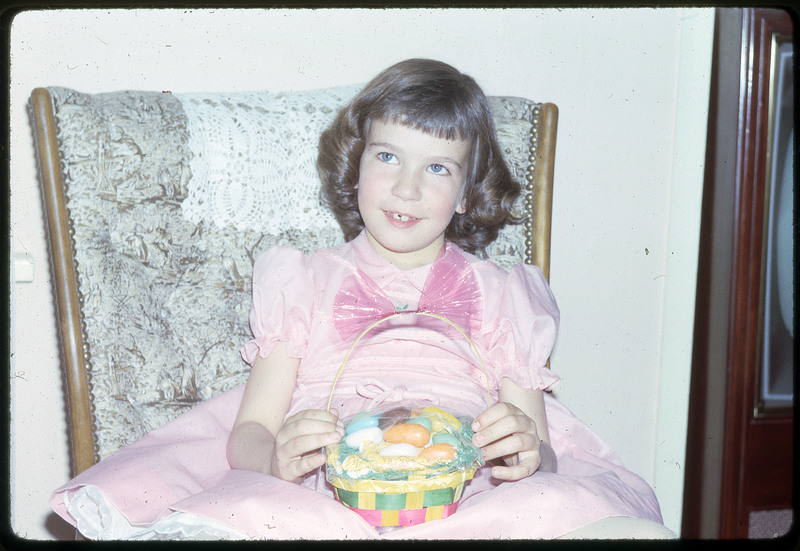 A photographic slide of a young girl in a fancy dress, holding a basket of Easter eggs.