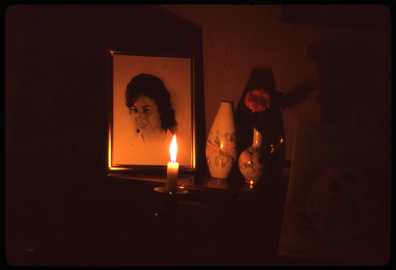 A photographic slide of a portrait of a young woman framed next to a vase and flower, lit by candlelight.