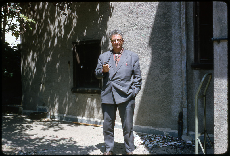 A photographic slide of a man with a pipe standing in front of a building.