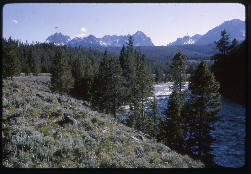 A photographic slide of a scenic view of a river running through forested mountains.