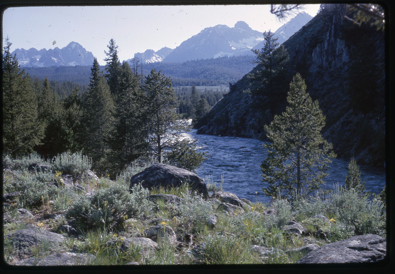 A photographic slide of a scenic view of a river running through forested mountains.