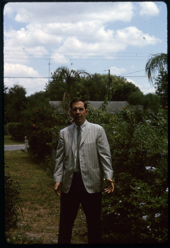 A photographic slide of a man in a suit standing in front of some greenery.