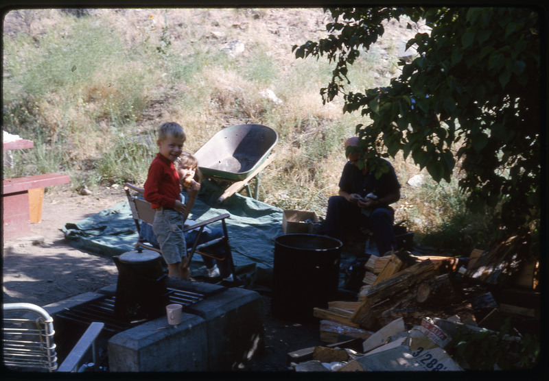 A photographic slide of two kids and an adult under shade in a campsite.