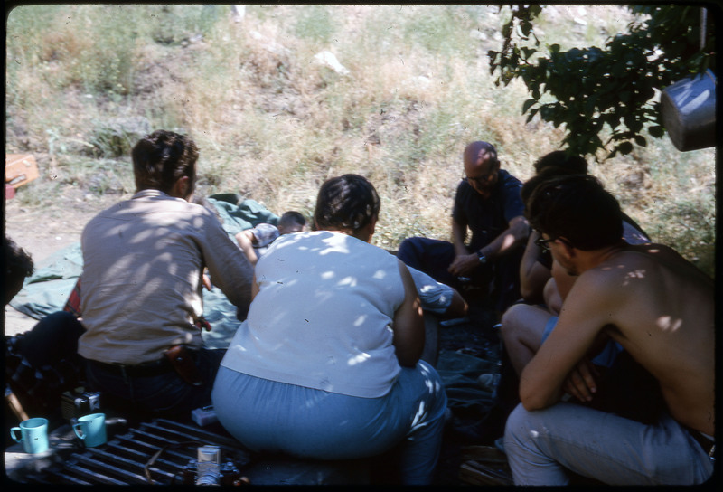 A photographic slide of a group of people huddled together under shade in a campsite.