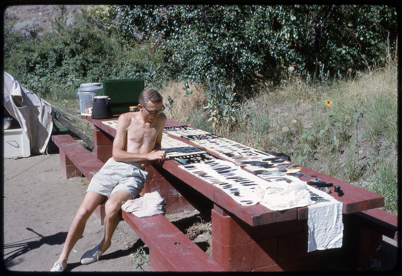 A photographic slide of Don E. Crabtree sitting on a park bench next to a collection of lithic artifacts.