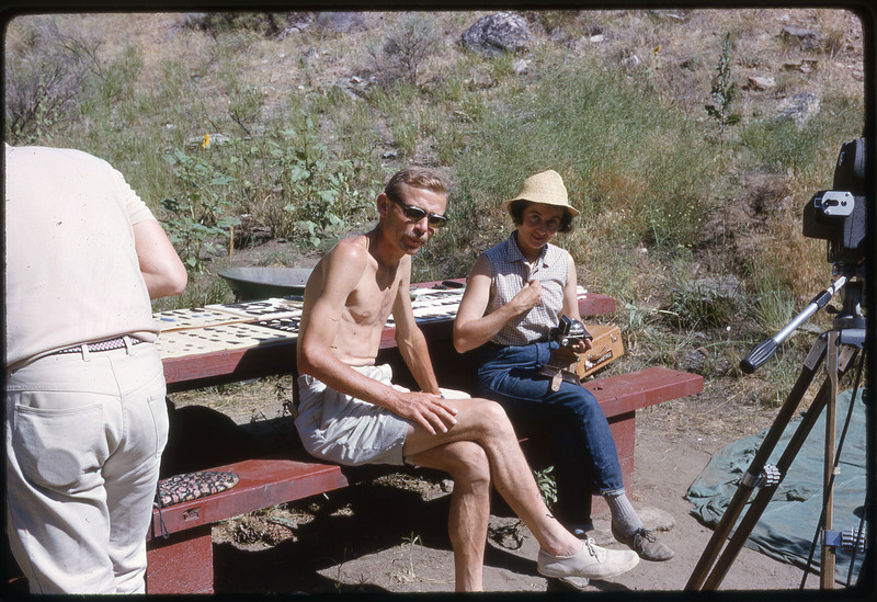 A photographic slide of Evelyn and Don E. Crabtree sitting together on a bench next to a collection of lithic artifacts.