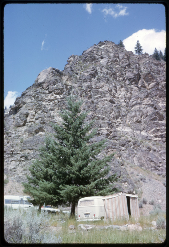 A photographic slide of a van in front of a steep, rocky hill.