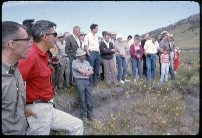 A photographic slide of a group of people gathered together outside next to some hills.