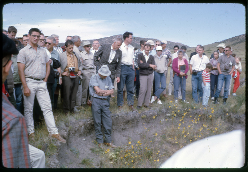 A photographic slide of a group of people gathered together outside next to some hills.