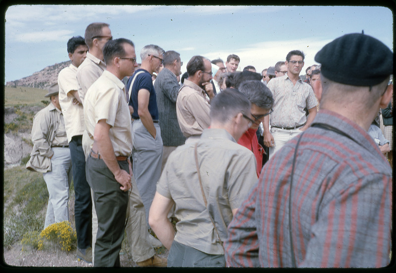 A photographic slide of a group of people gathered together outside next to some hills.