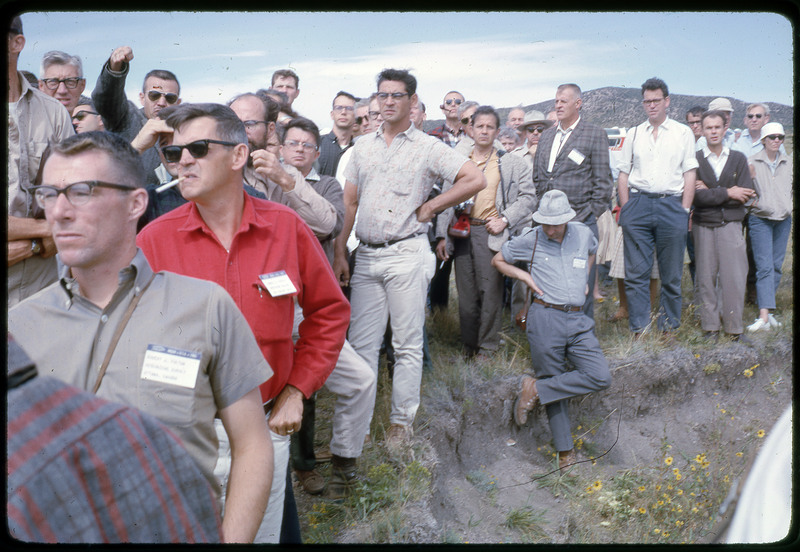 A photographic slide of a group of people gathered together outside next to some hills.