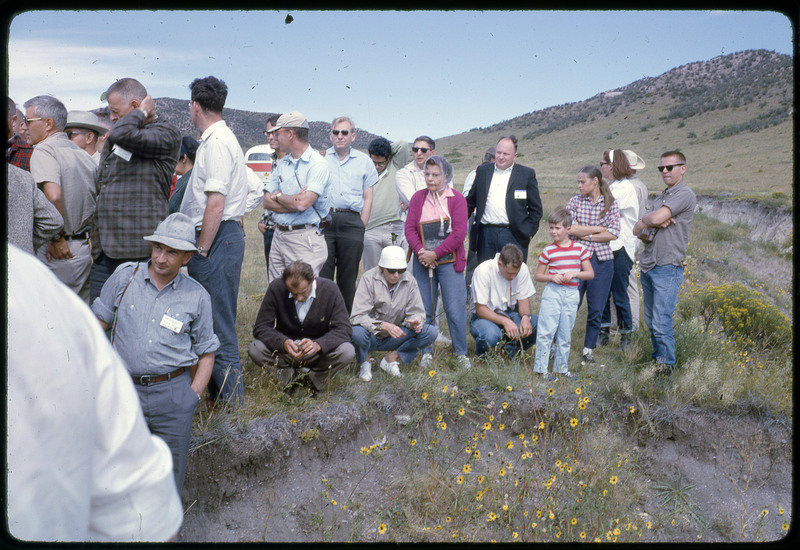 A photographic slide of a group of people gathered together outside next to some hills.