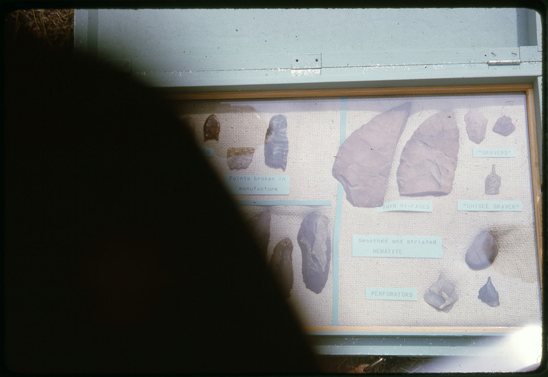 A photographic slide of a obscured view of a display of lithic tools and bifaces.