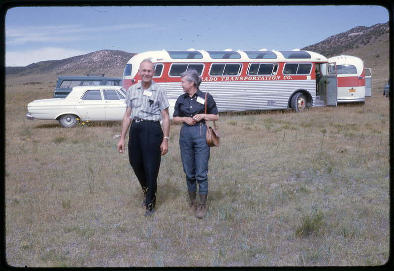 A photographic slide of a man and a woman smiling together in front of a bus in the hills.