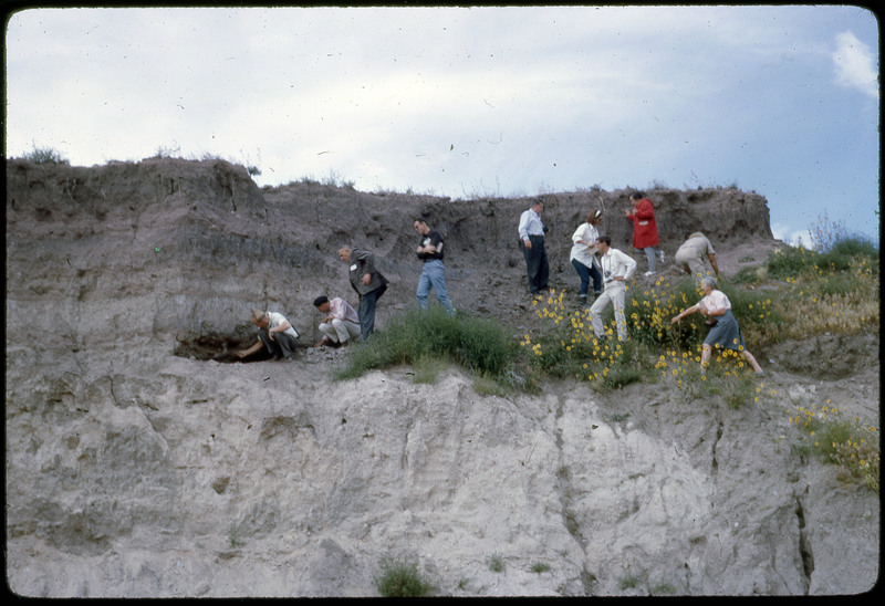 A photographic slide of a group of people gathered together on a steep slope, observing strata layers.