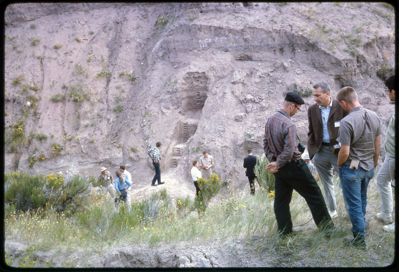 A photographic slide of a group of people gathered together on a steep slope, observing strata layers.