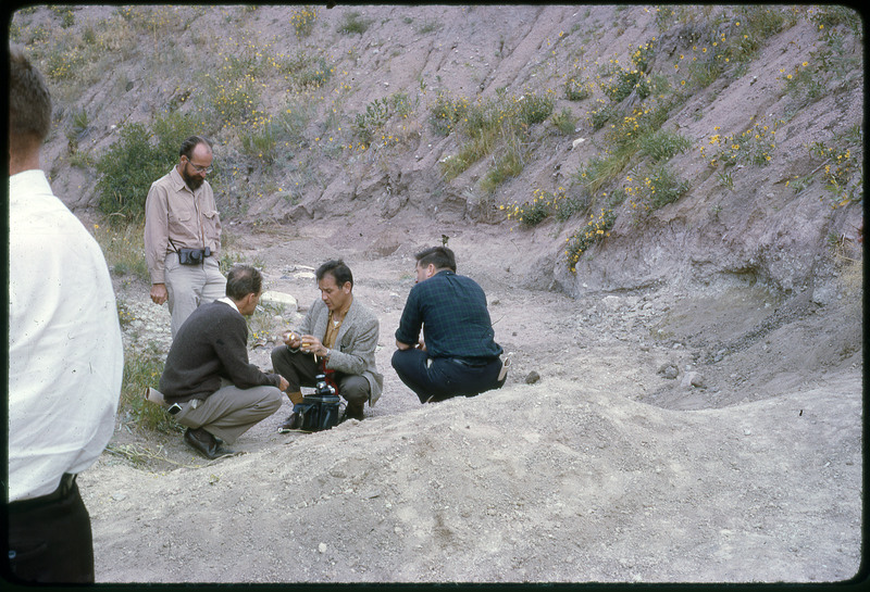 A photographic slide of a group of people gathered together outside next to some hills.