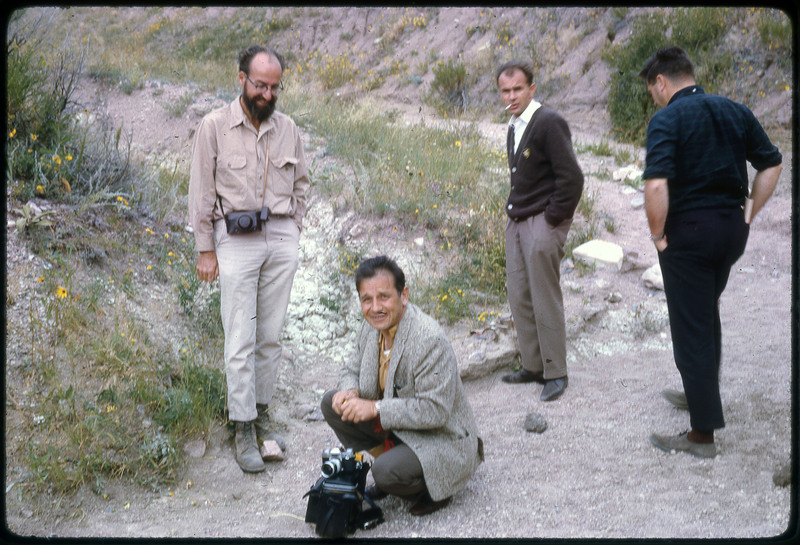 A photographic slide of four men standing next to some hills with cameras.