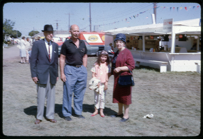 A photographic slide of a blurry view of two men, a woman, and a child stand next to a series of foodstands.