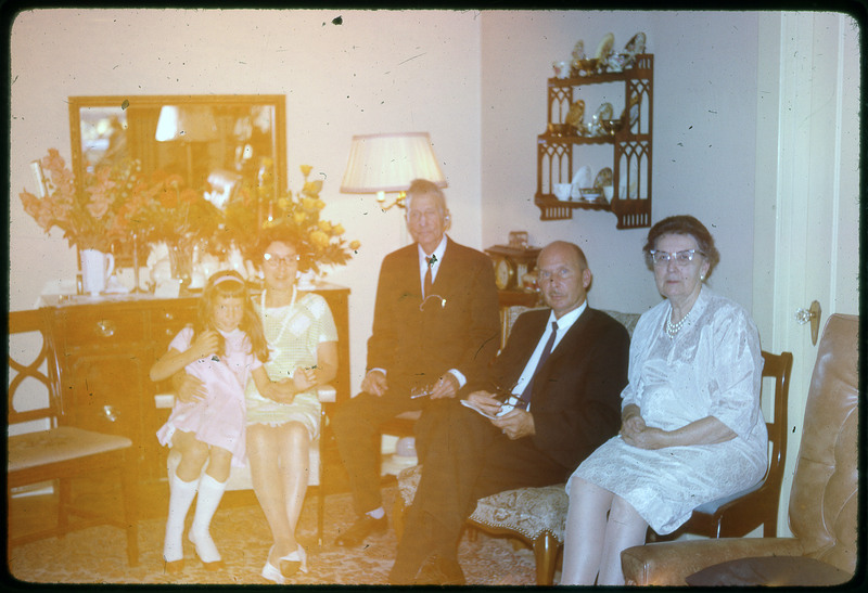 A photographic slide of a distorted view of two men, two women, and a child seated inside for a group picture.