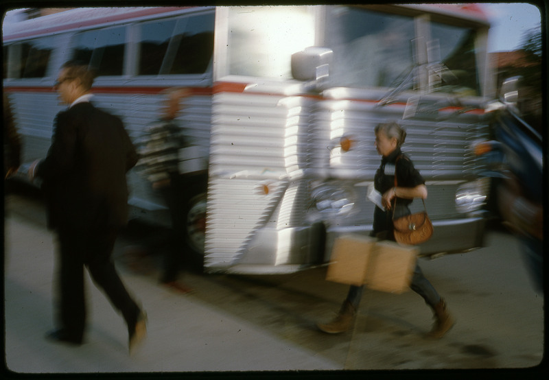 A photographic slide of a blurry view of people walking around an open bus.