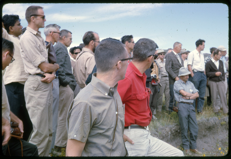 A photographic slide of a group of people gathered together outside next to some hills.