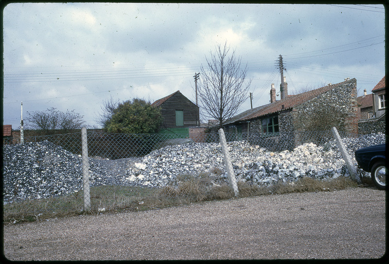 A photographic slide of a fenced-off pile of rocks next to a stone building.