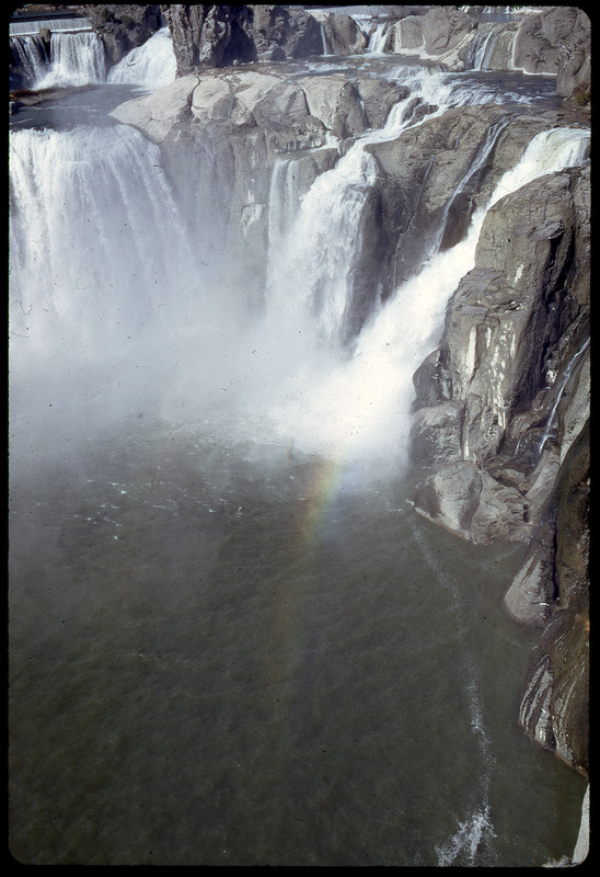 A photographic slide of a scenic view of a series of waterfalls with a rainbow visible within the mist.