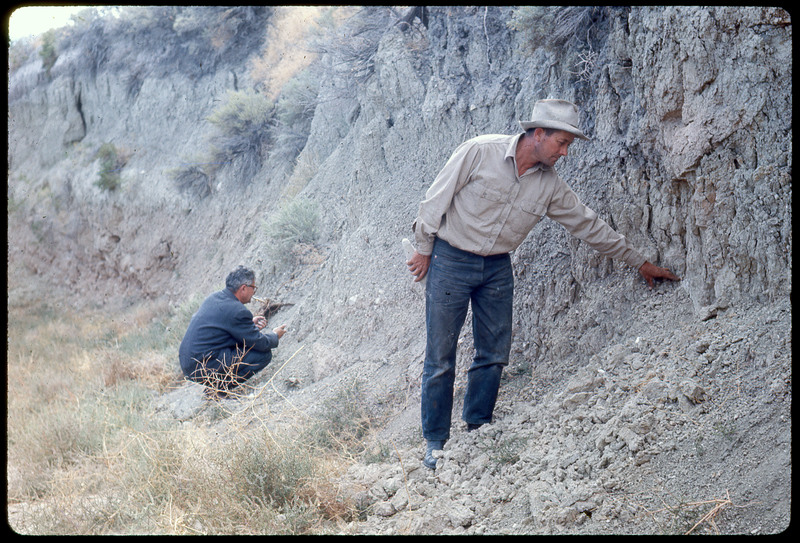 A photographic slide of two men surveying the side of a cliff.