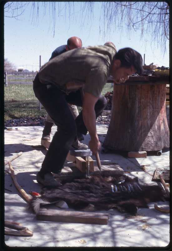 A photographic slide of two men working over an animal pelt with wooden tools.