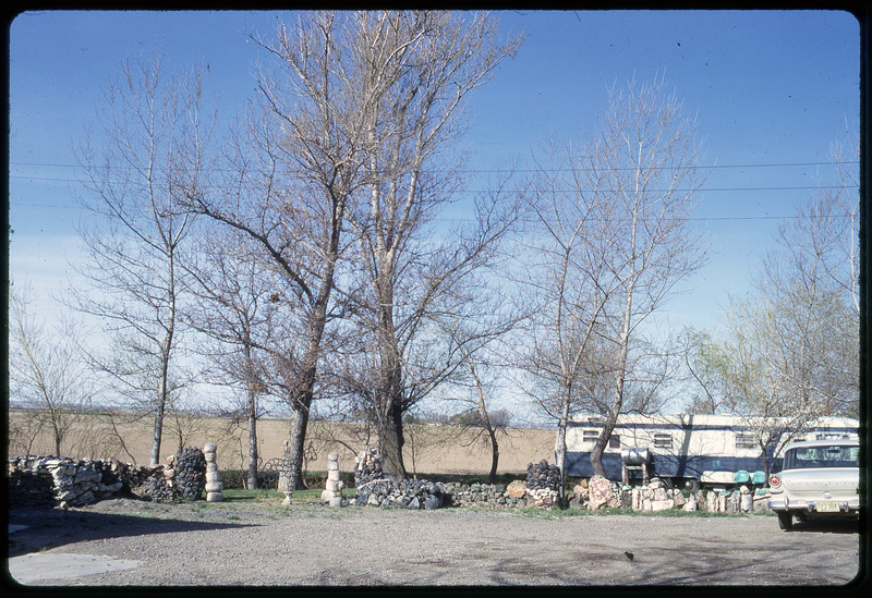 A photographic slide of a RV parked outside behind a short stone wall.