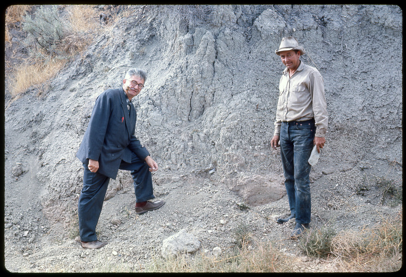 A photographic slide of two men smiling next to a cliffside. One is smoking a pipe.