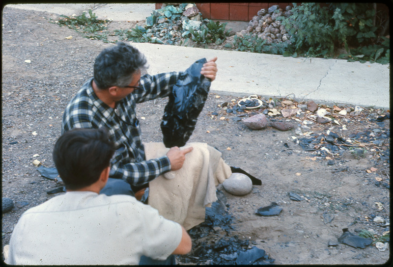 A photographic slide of a man holding a large obsidian biface on his knee.