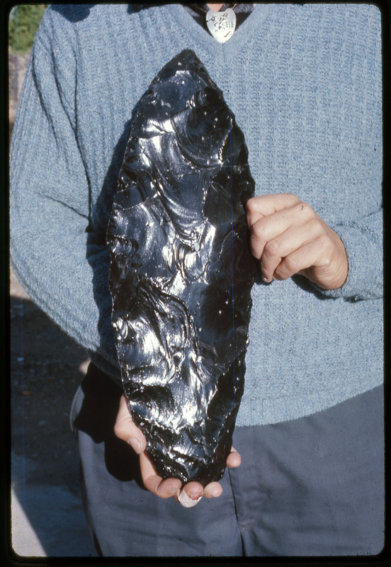 A photographic slide of a person holding a large obsidian biface.