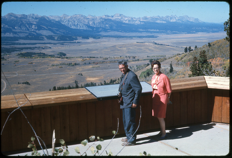 A photographic slide of a man and a woman standing over a scenic mountainside view.