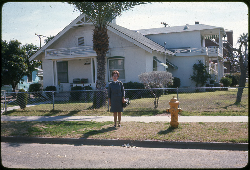 A photographic slide of a woman standing in front of a large white house.