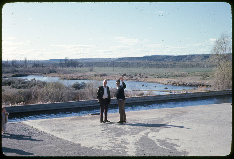 A photographic slide of two men posing in front of a river, with a child barely in frame.