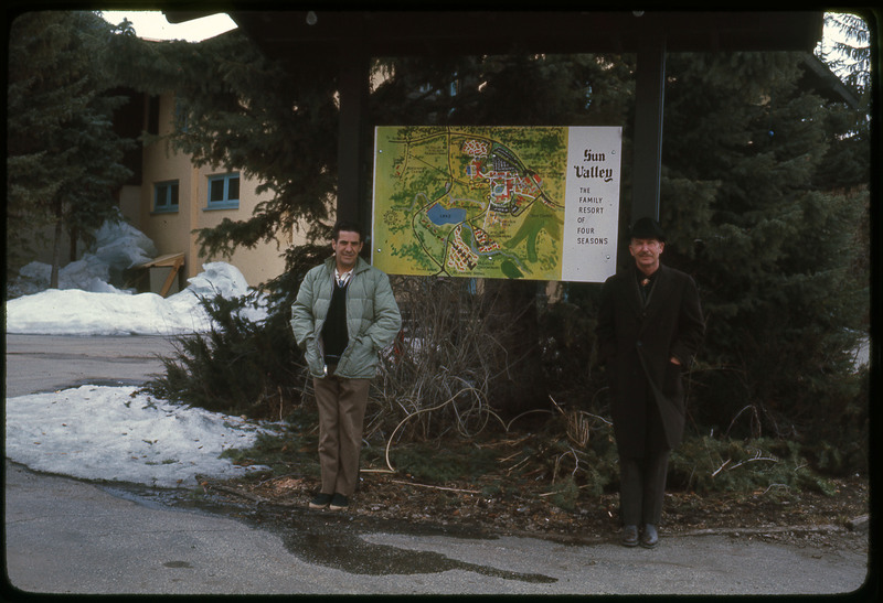 A photographic slide of two men standing in front of a sign with a map of Sun Valley Resort.