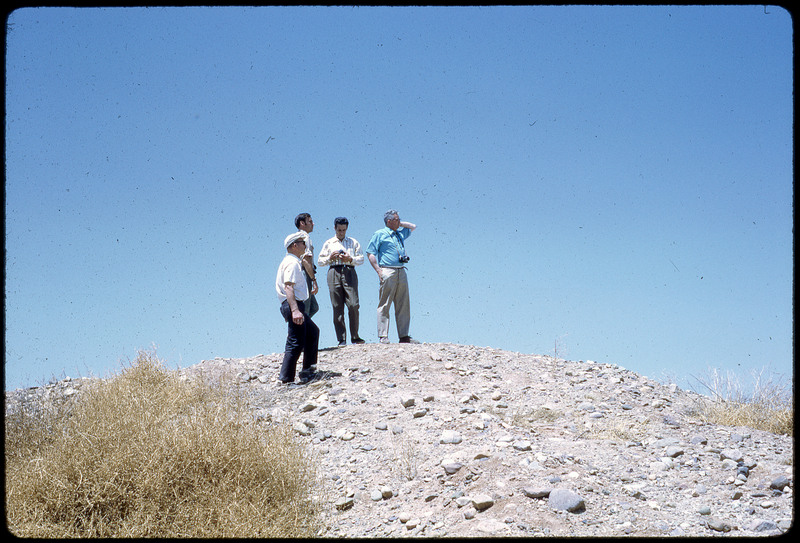 A photographic slide of four men standing on top of a rocky hill.