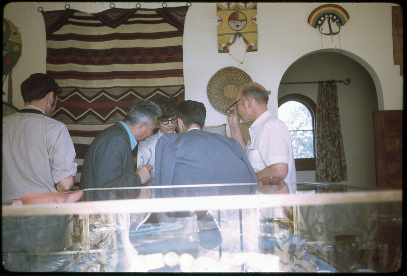 A photographic slide of five people gathered over an unknown item in front of a glass display case.