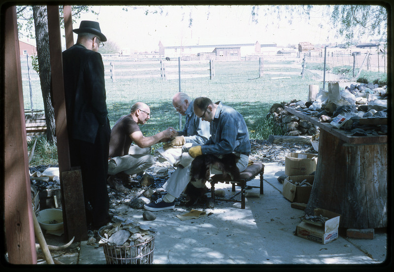 A photographic slide of three men flintknapping on a porch while a fourth man watches.