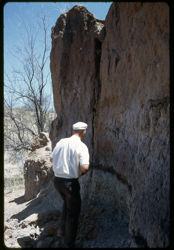 A photographic slide of a man observing the side of a large rock.